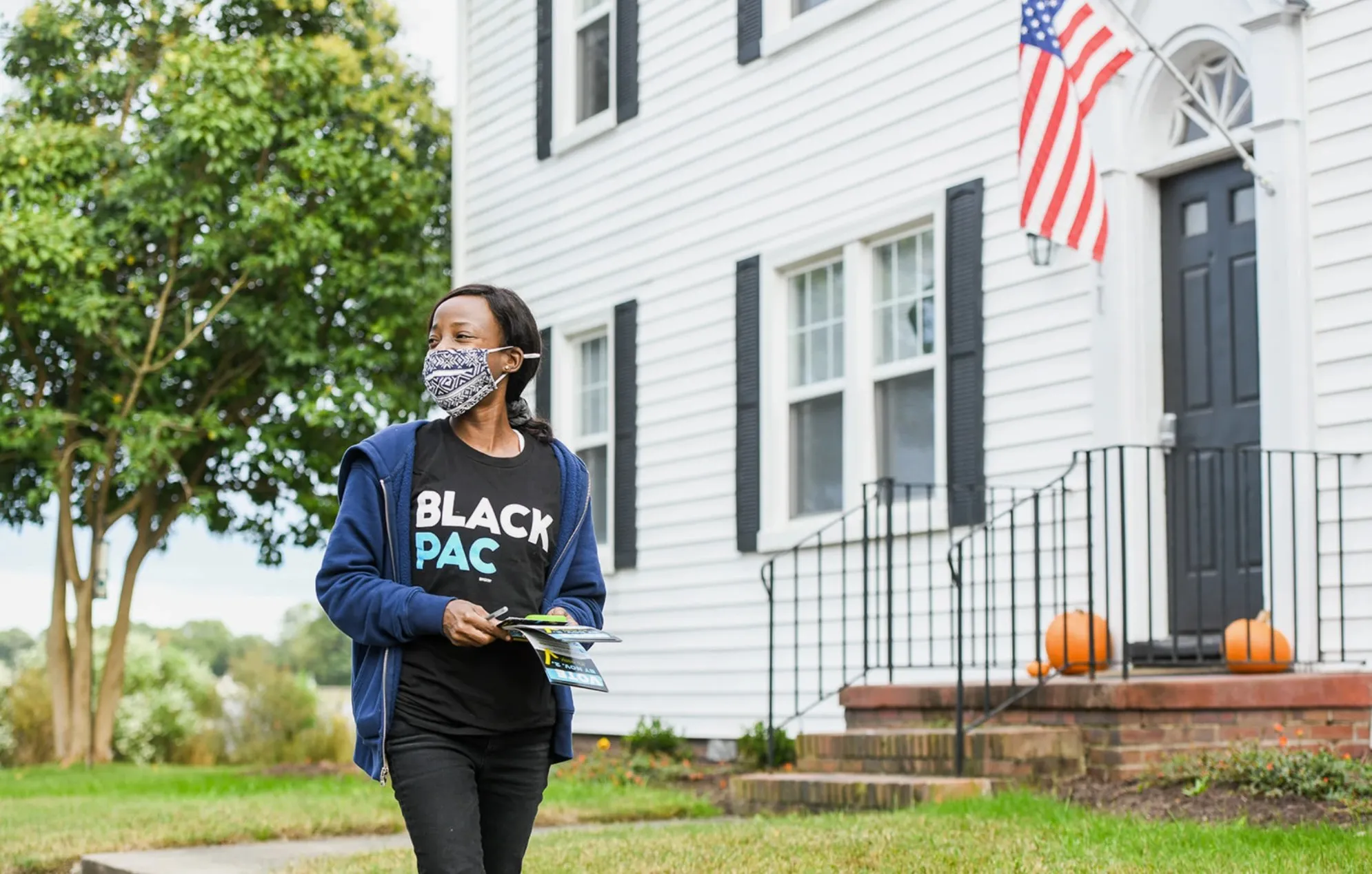 A BlackPAC canvasser with voter guides walking past a house flying an American flag